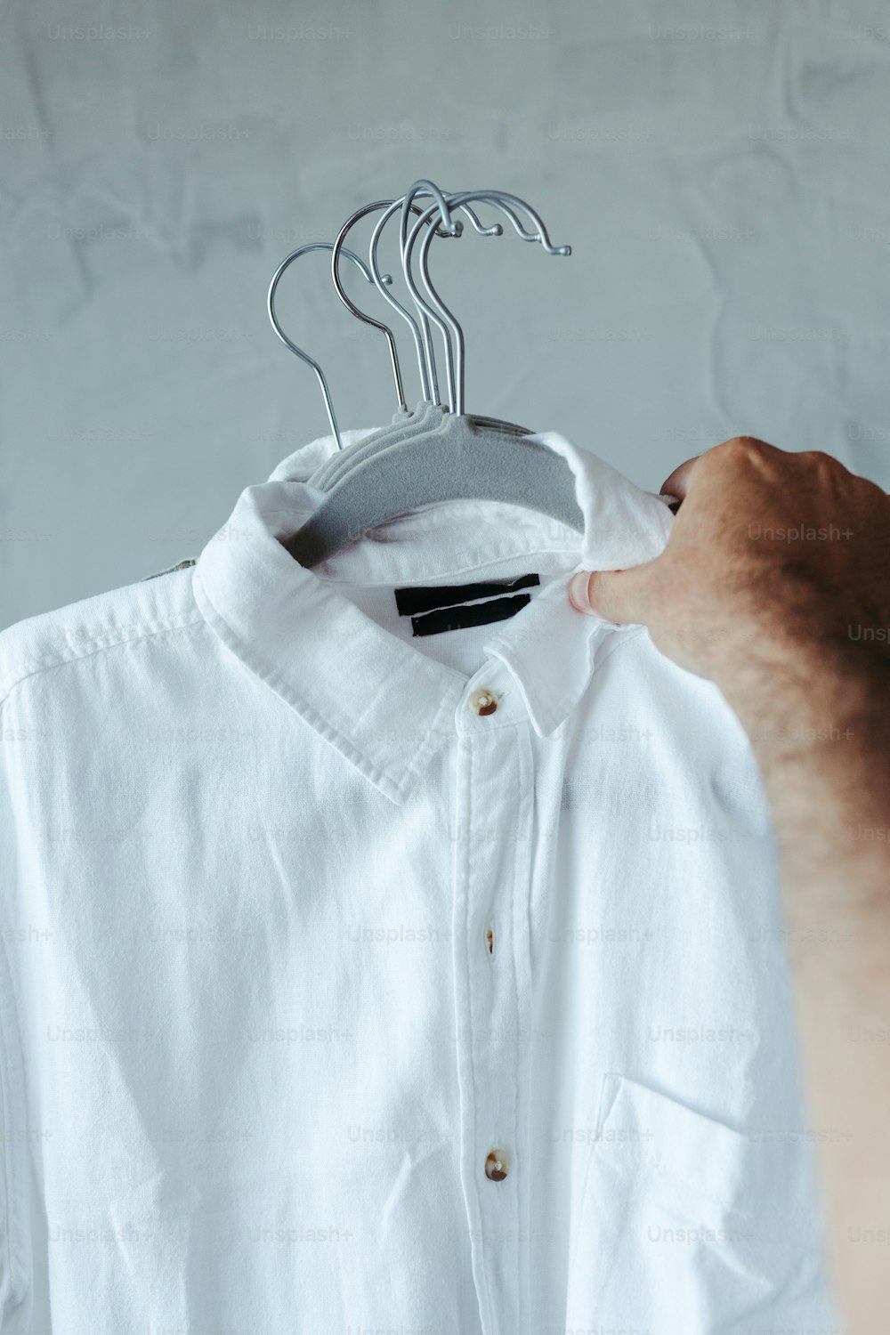 eine Person, die ein weißes Hemd auf einem Kleiderbügel hält