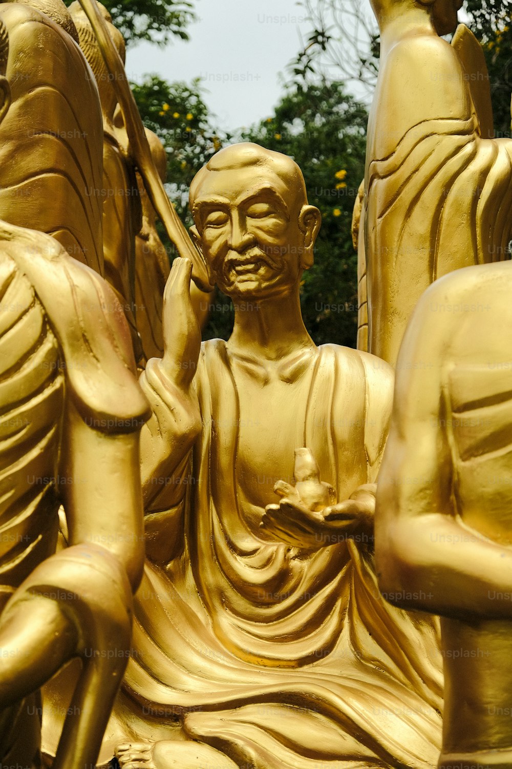 a golden statue of buddhas sitting in front of a tree