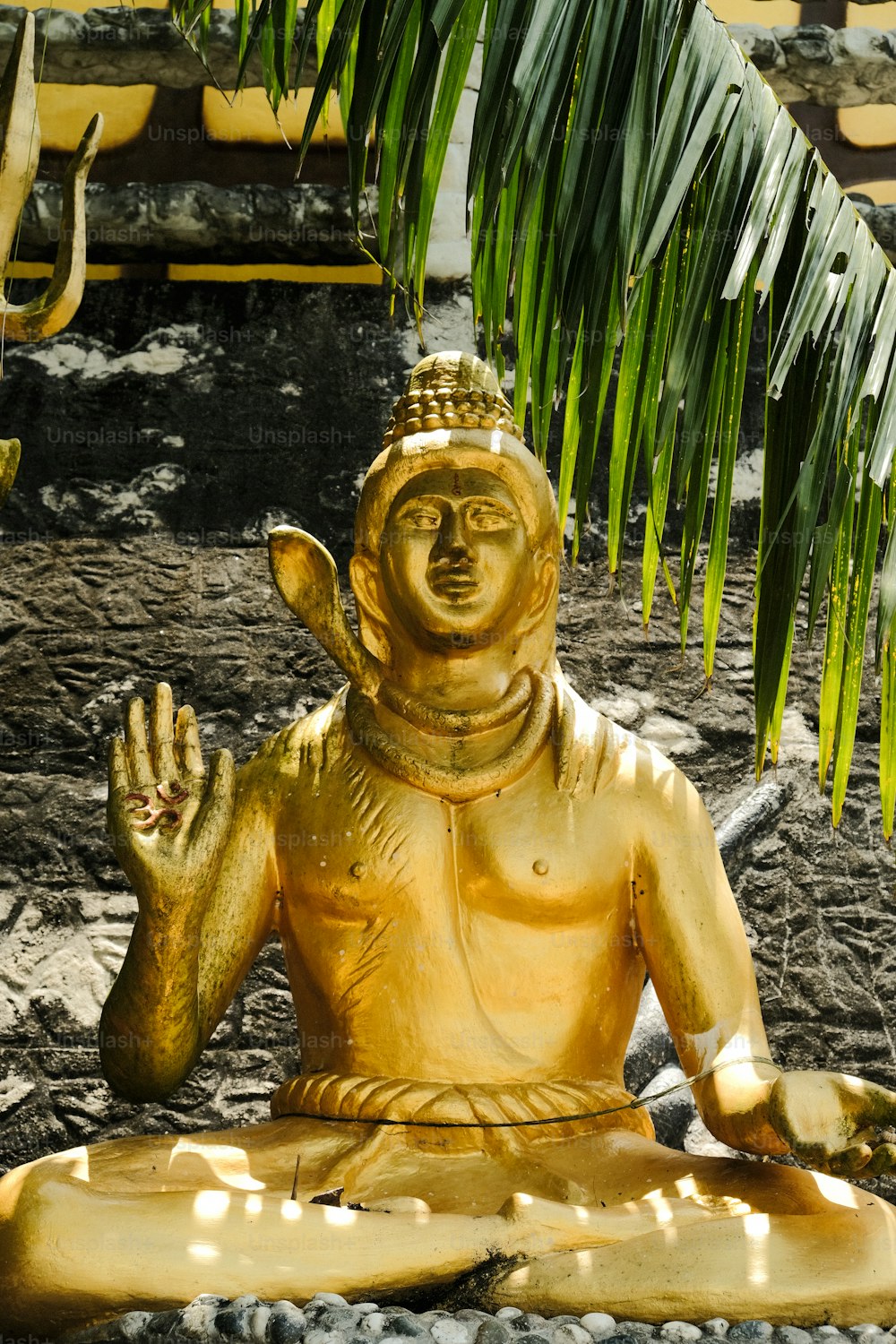 a golden buddha statue sitting under a palm tree