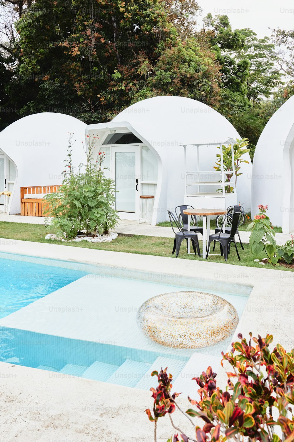 una piscina frente a un edificio blanco con una mesa y sillas