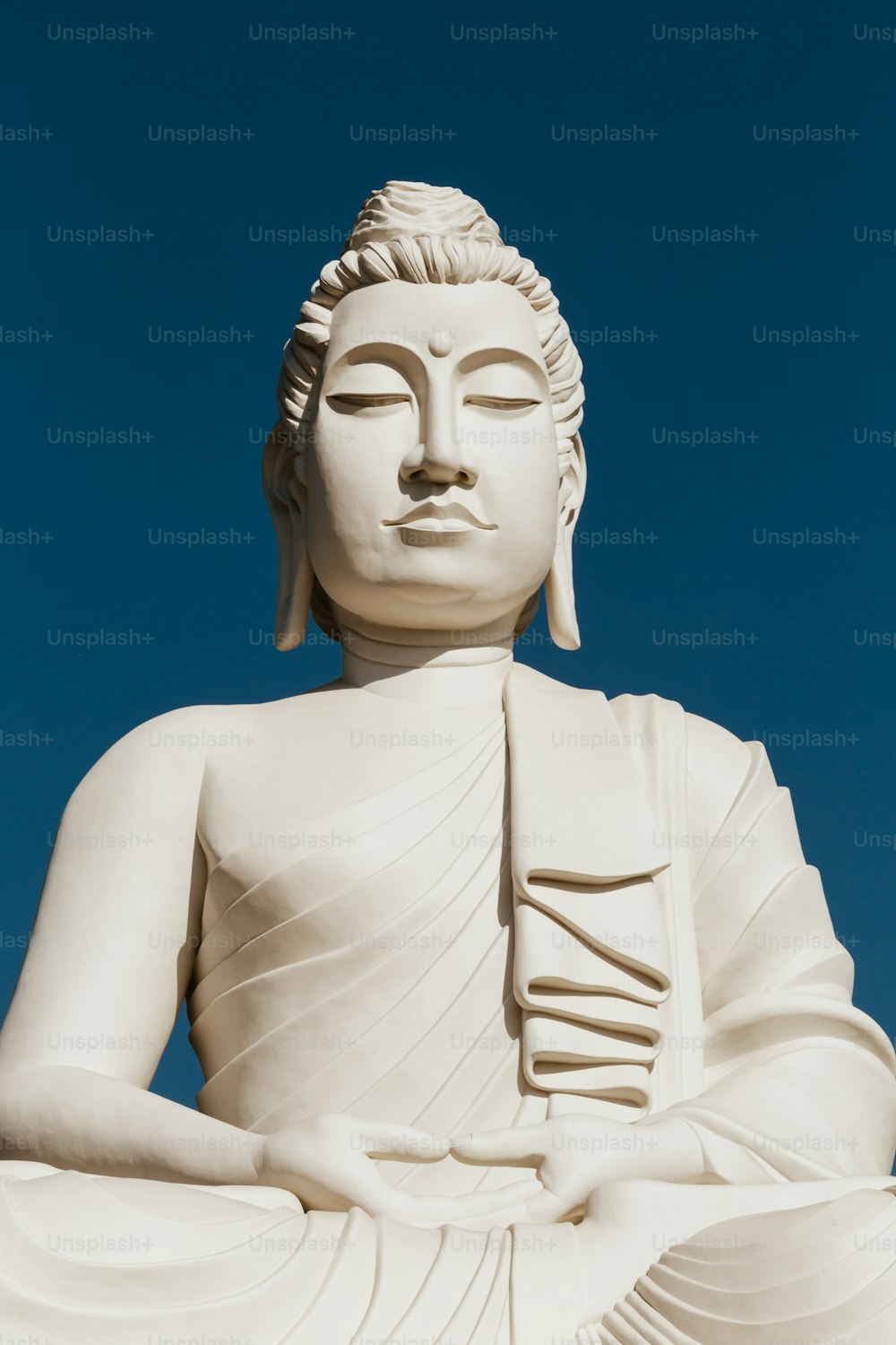 uma grande estátua branca de buddha sentada no topo de uma colina