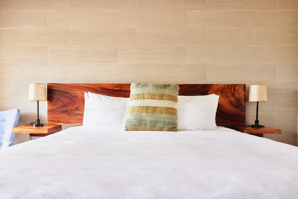 una cama con sábanas y almohadas blancas y una cabecera de madera