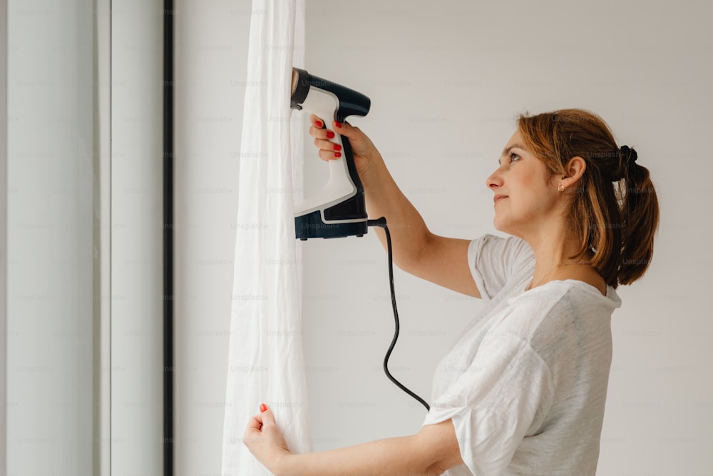 a woman using a hair dryer on a curtain
