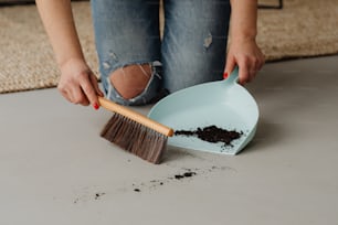 une femme nettoie un sol avec une pelle à poussière et une brosse
