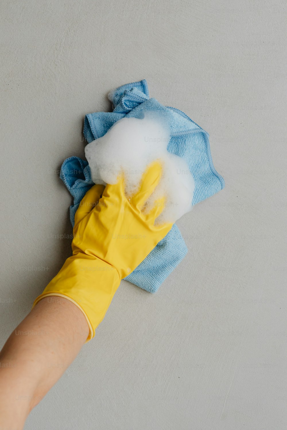 a person's hand wearing yellow rubber gloves and cleaning cloth