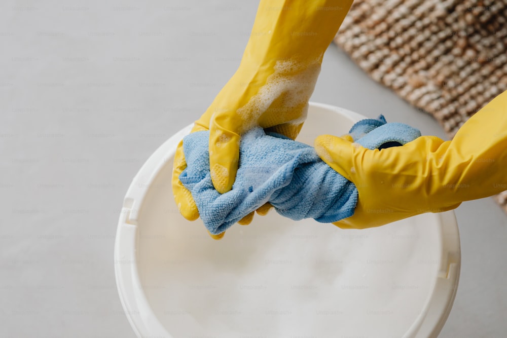 eine Person in gelben Handschuhen und blauen Handschuhen, die eine weiße Schüssel reinigt