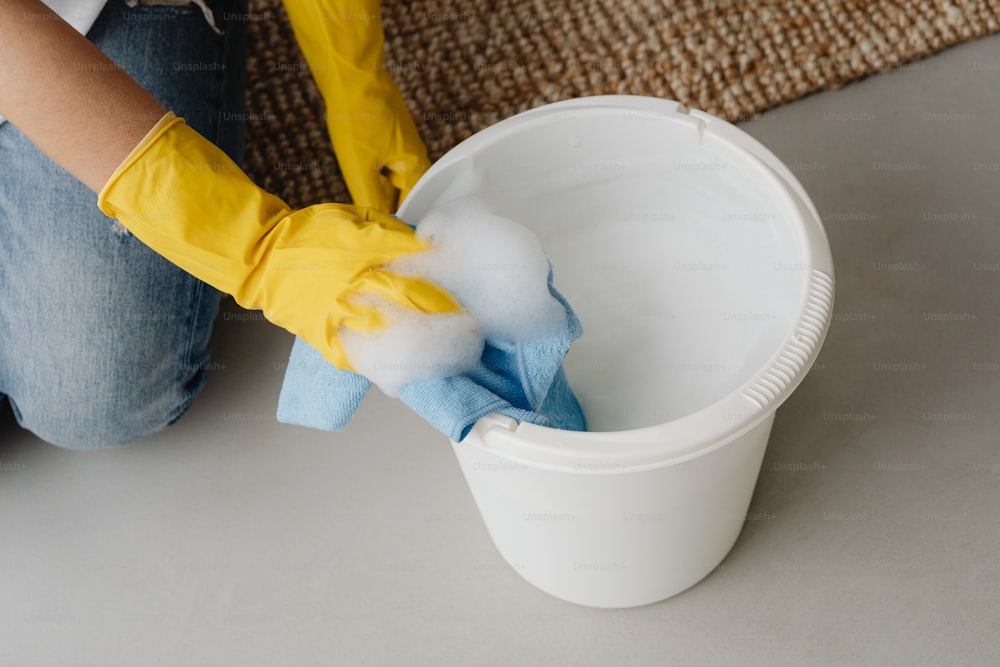 a person in yellow gloves is cleaning a bucket