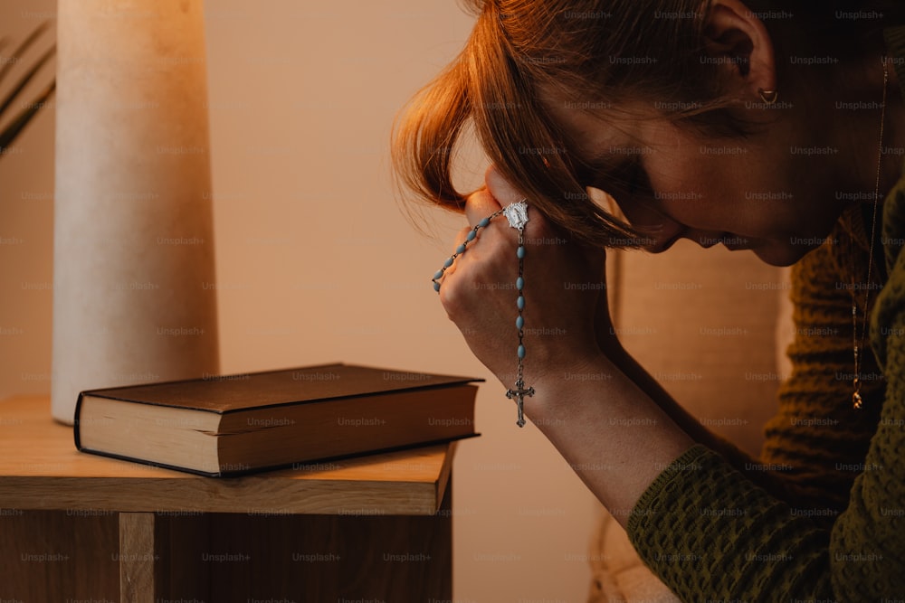 a woman holding a rosary next to a book