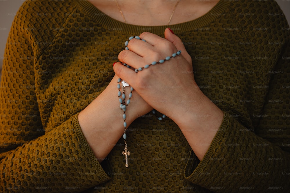 a woman wearing a green sweater holding a rosary