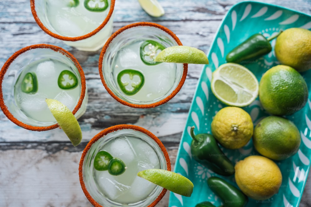 three glasses filled with drinks and limes on a table