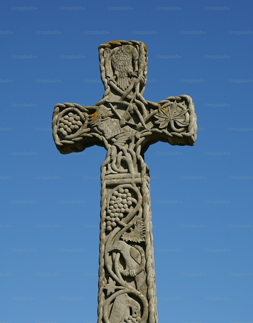 une croix de pierre avec des sculptures dessus contre un ciel bleu