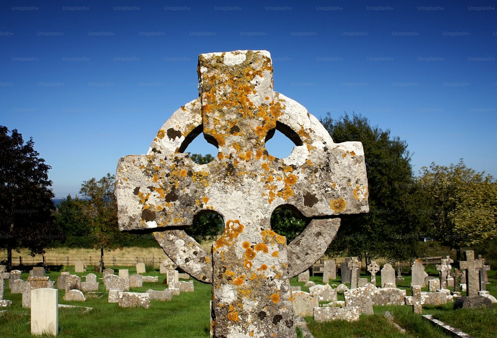 uma grande cruz de pedra em um cemitério com árvores no fundo