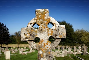 uma grande cruz de pedra em um cemitério com árvores no fundo