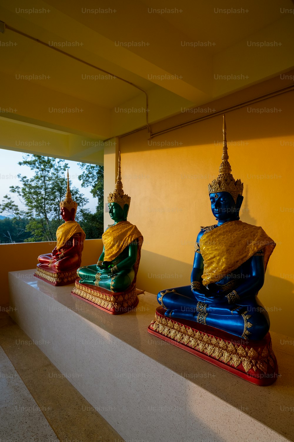 Trois statues de Bouddhas assis sur un rebord