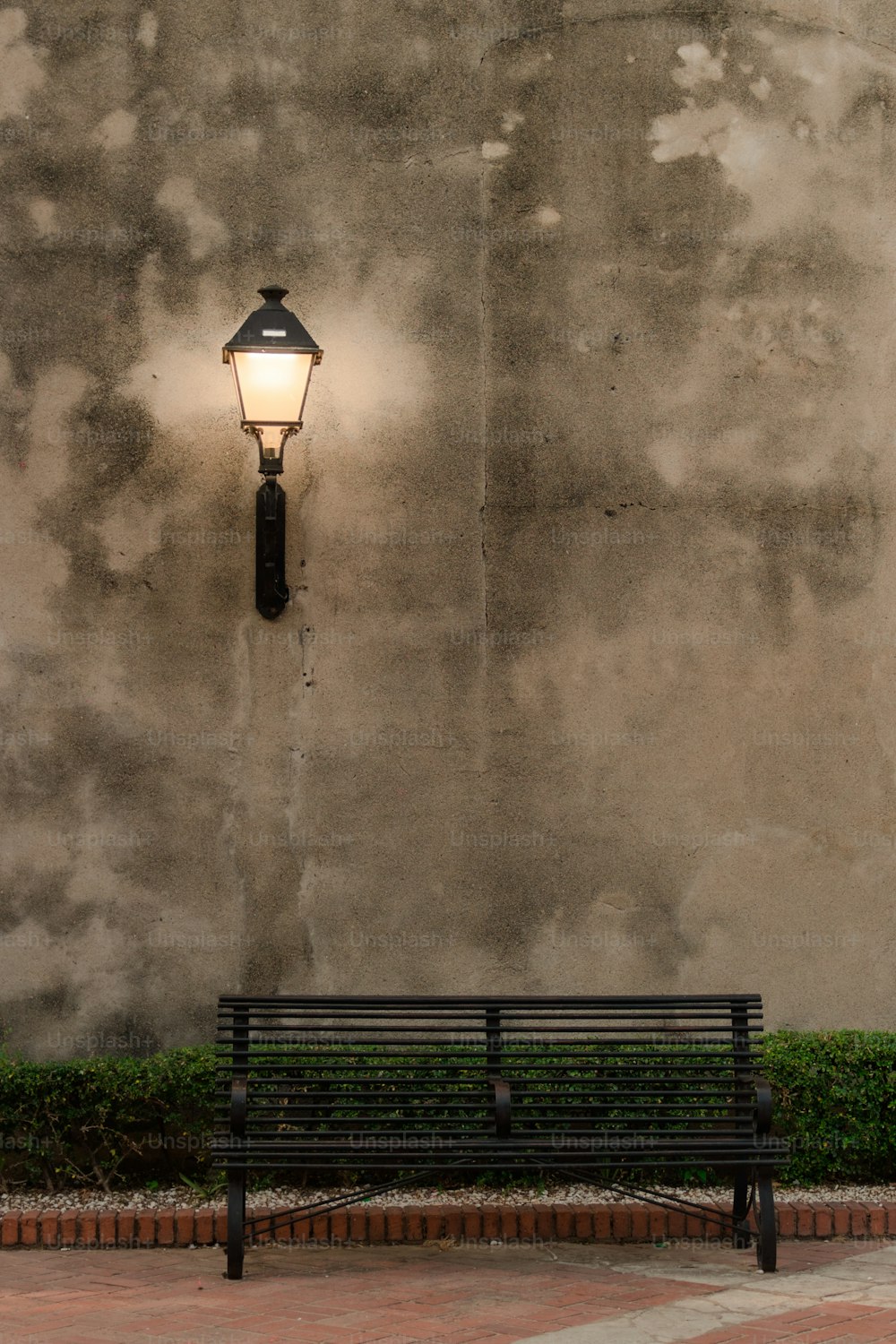 a bench sitting in front of a wall with a light on it