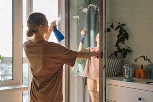 a woman cleaning a window with a sprayer