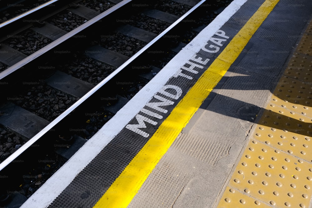 a train track with a yellow line and a sign that says mind the gap