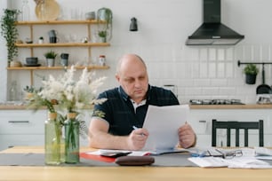Un hombre sentado en una mesa de cocina mirando un pedazo de papel