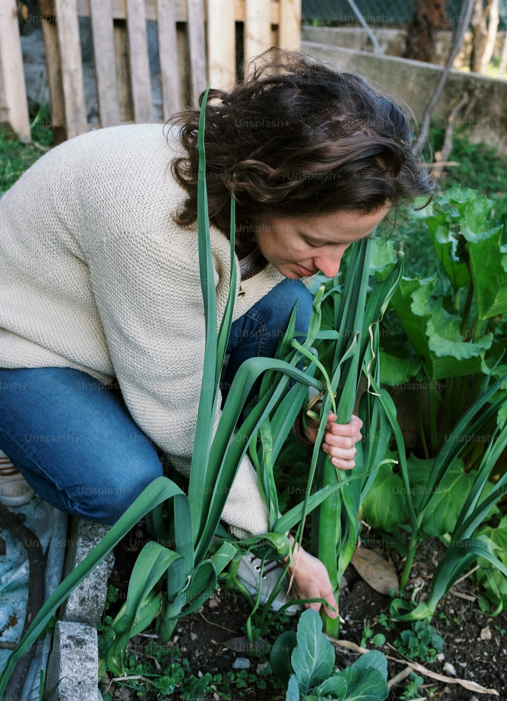 a woman kneeling down to pick up some plants