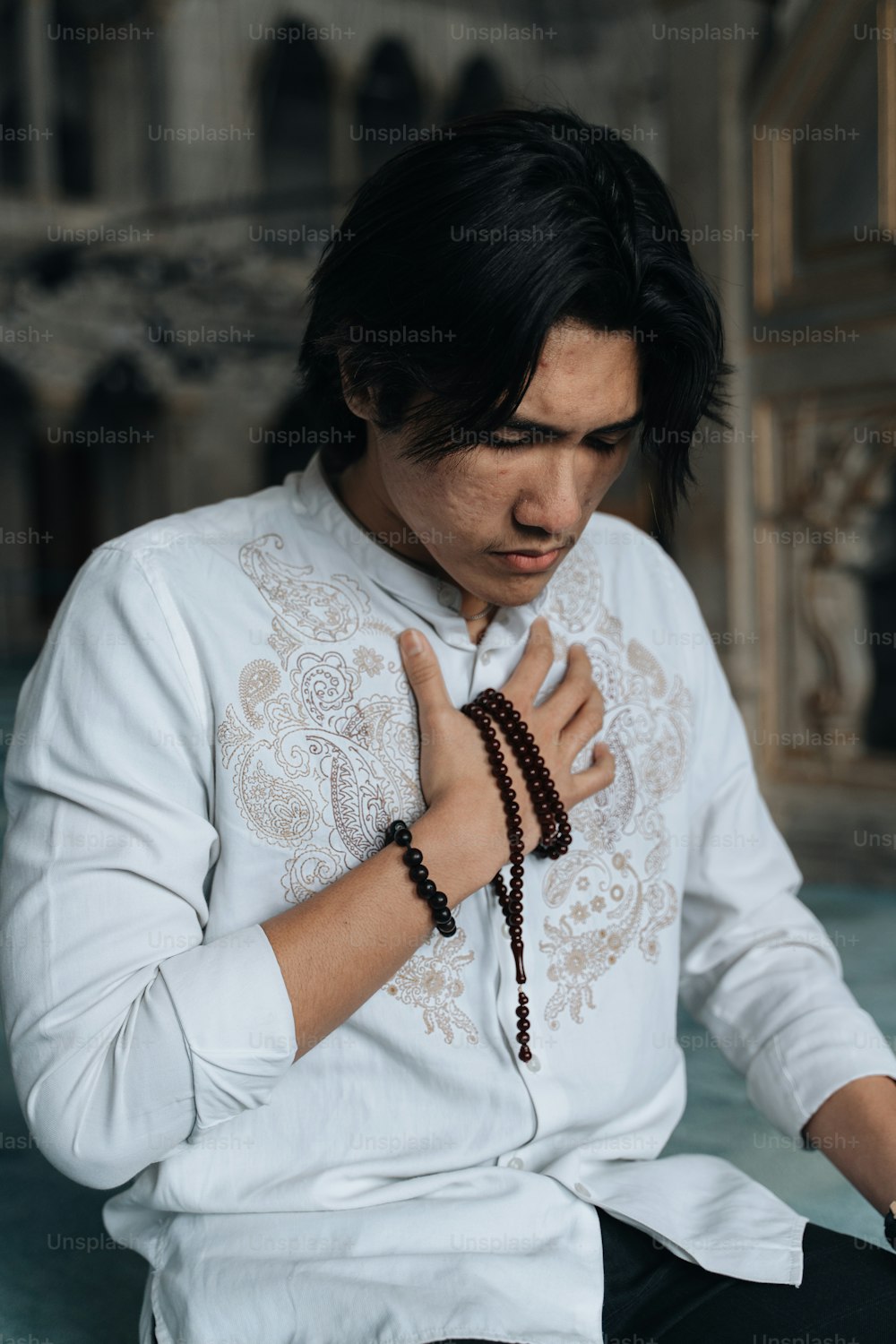 a man in a white shirt and beaded necklace