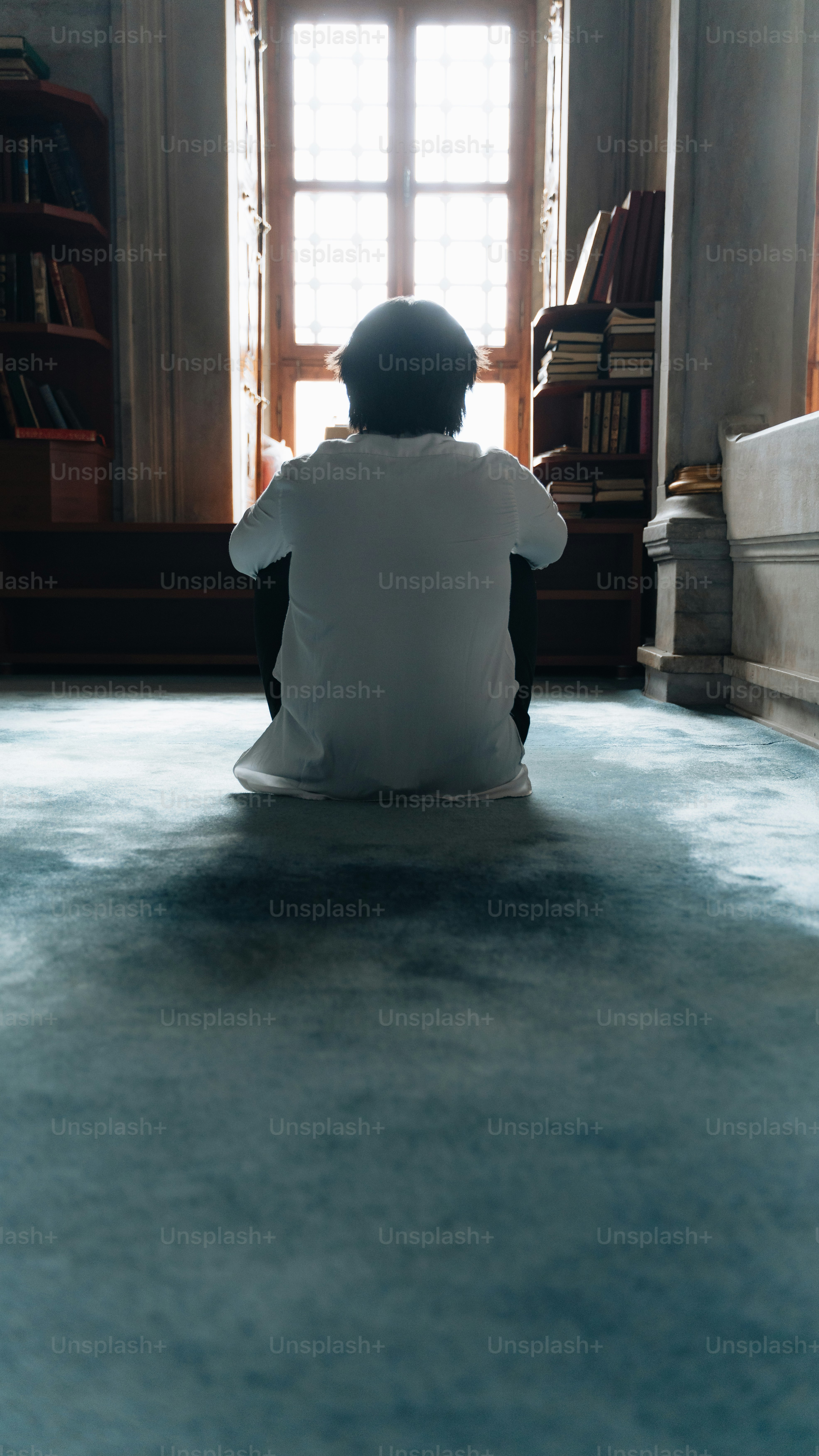 Una persona sentada en el suelo frente a una ventana