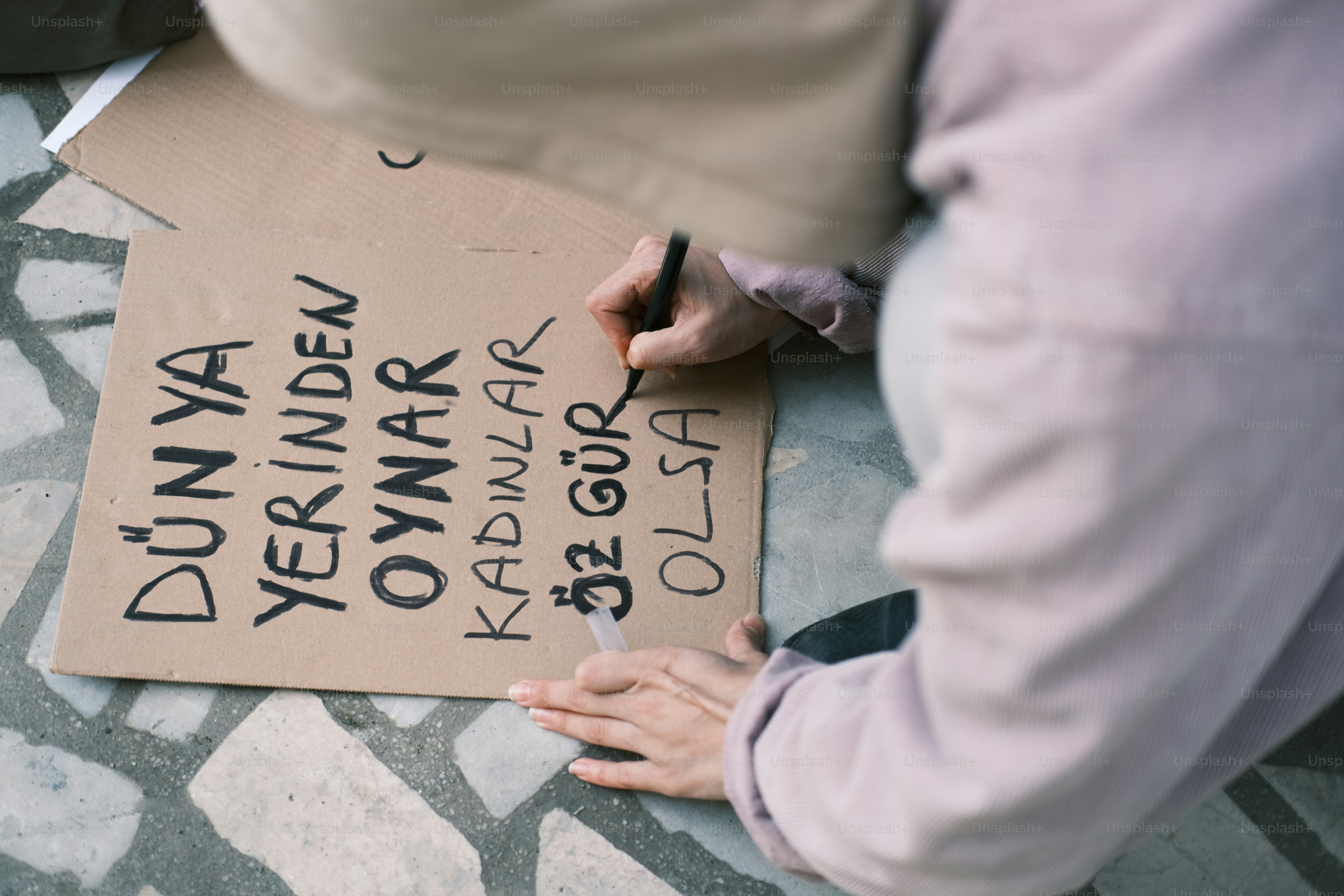 a person writing on a cardboard sign on the ground