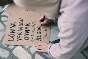 a person writing on a cardboard sign on the ground