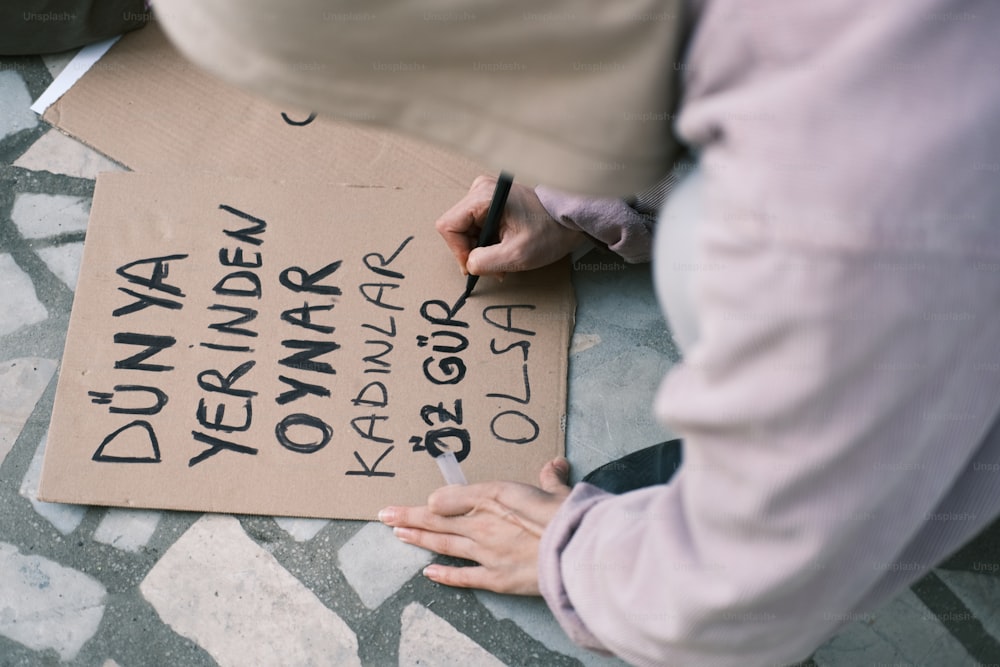 une personne écrivant sur une pancarte en carton au sol