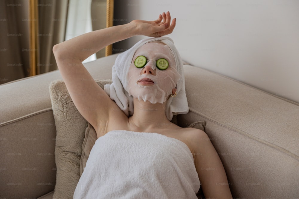 Une femme avec des tranches de concombre sur le visage et une serviette sur la tête