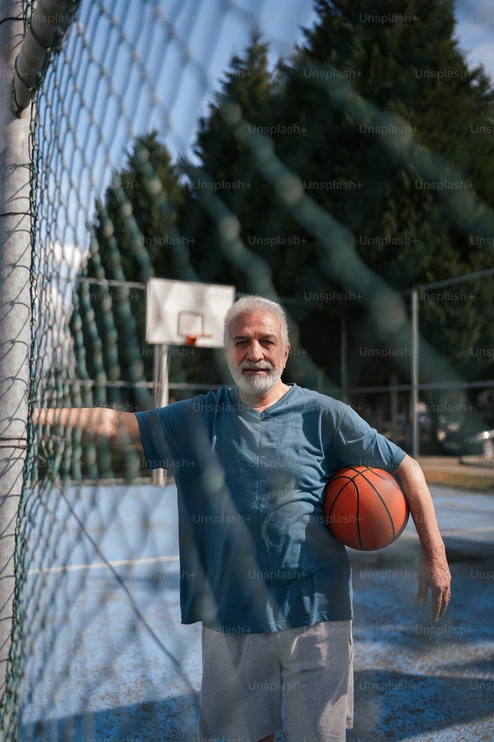 a man holding a basketball standing next to a fence