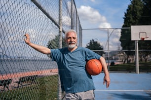 a man holding a basketball standing next to a fence
