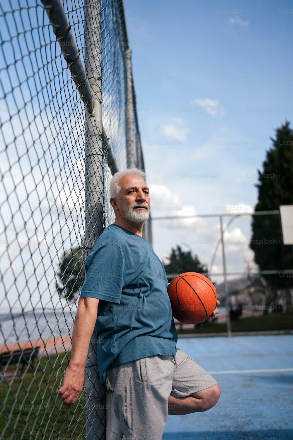 a man leaning against a fence holding a basketball