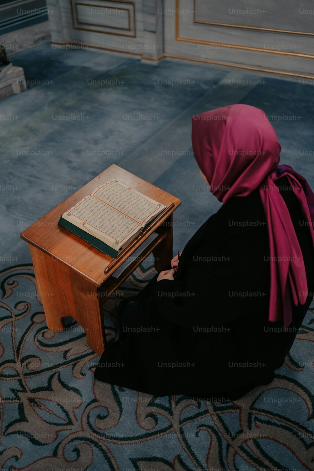 Eine Frau in einem schwarzen Kleid sitzt an einem Schreibtisch mit einem Buch darauf