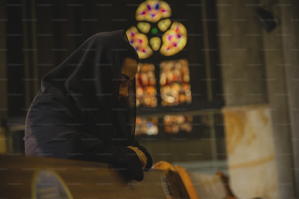 uma pessoa em um capuz preto sentado na frente de um vitral