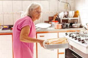 an older woman holding a pan of bread in a kitchen