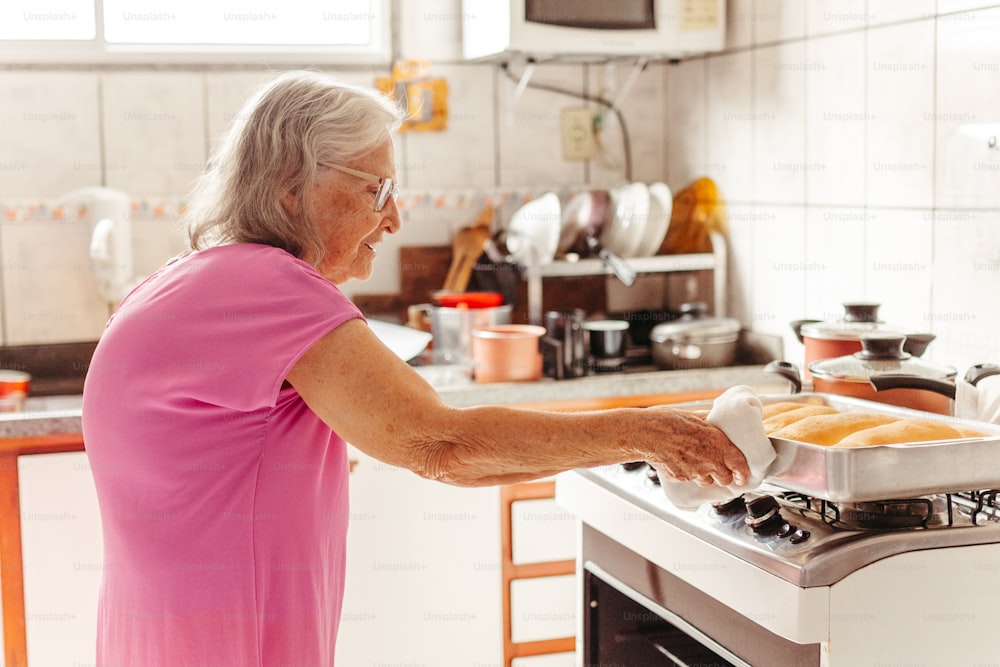 Una mujer con una camisa rosa está poniendo una sartén de comida en el horno