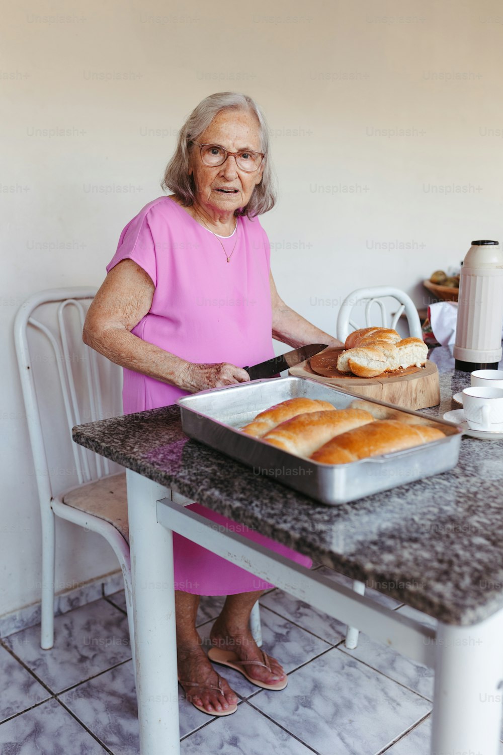 a woman in a pink dress standing in front of a pan of bread