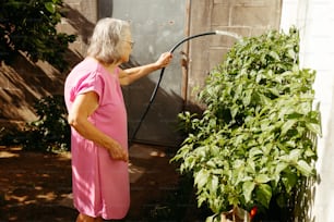 uma mulher em um vestido rosa está regando plantas