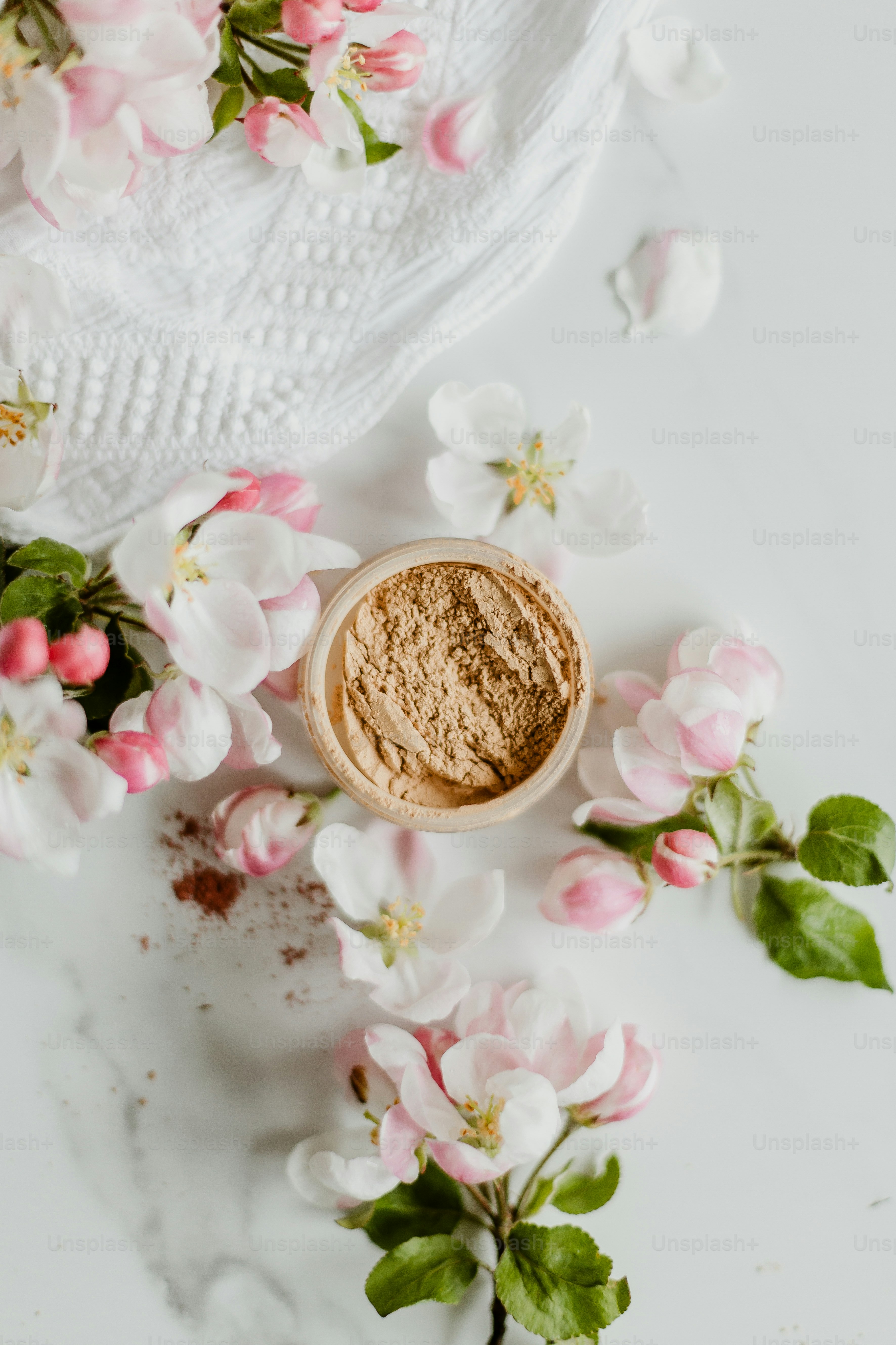 a bowl of powder next to flowers on a white surface