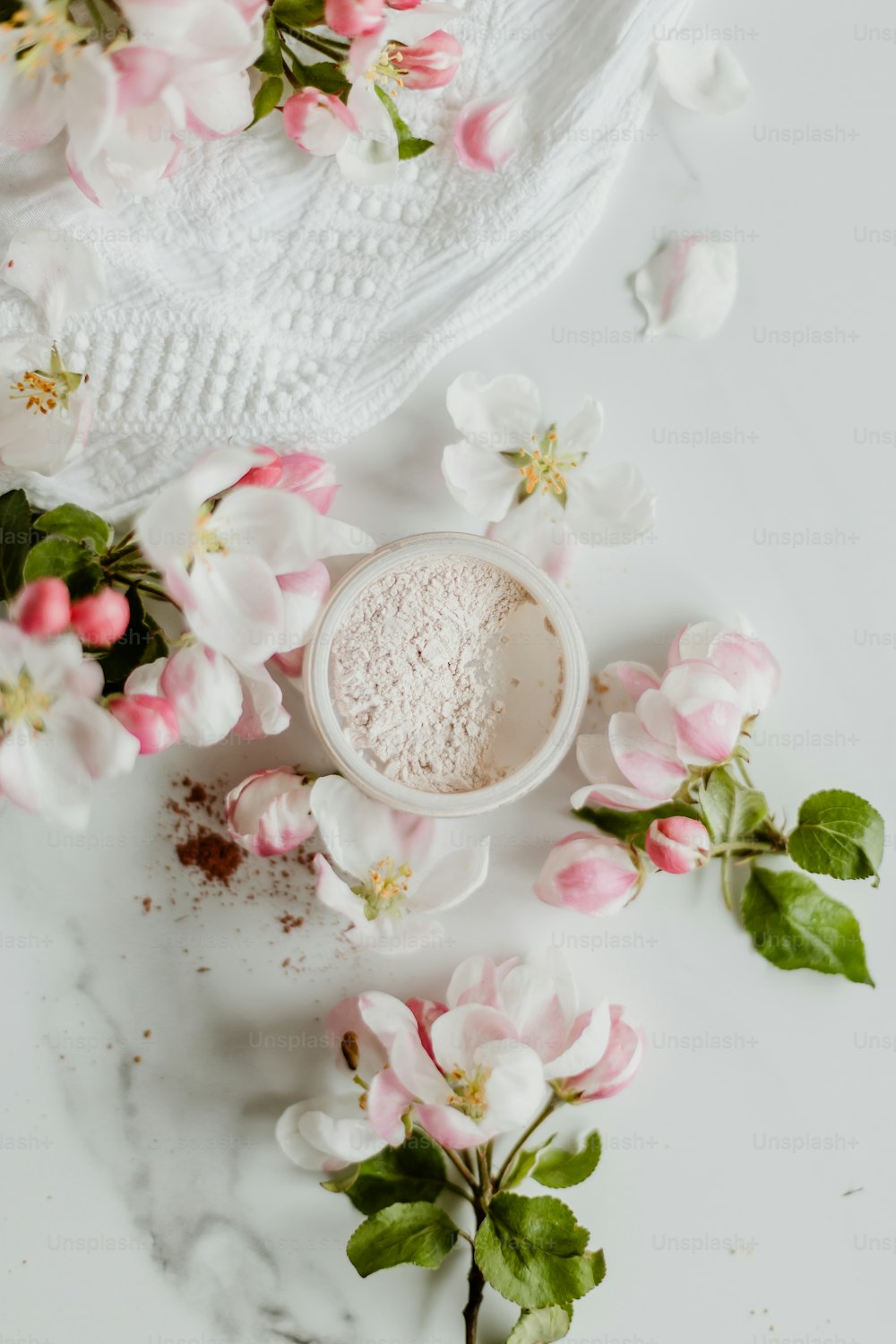 um pó branco em uma tigela cercada por flores cor-de-rosa