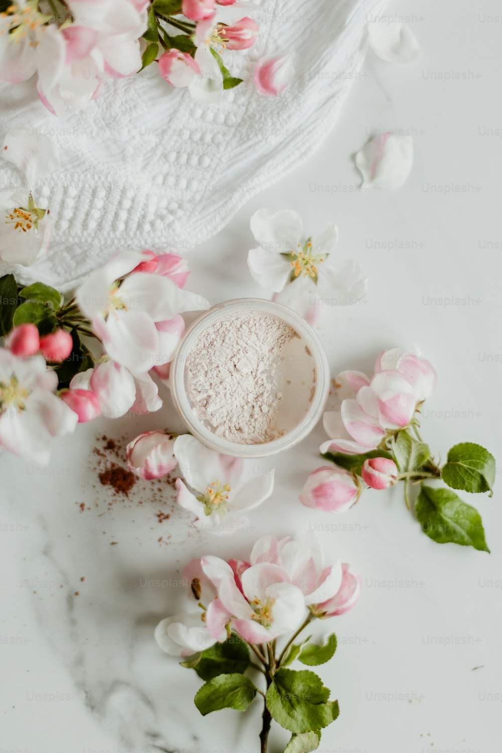 une poudre blanche dans un bol entouré de fleurs roses