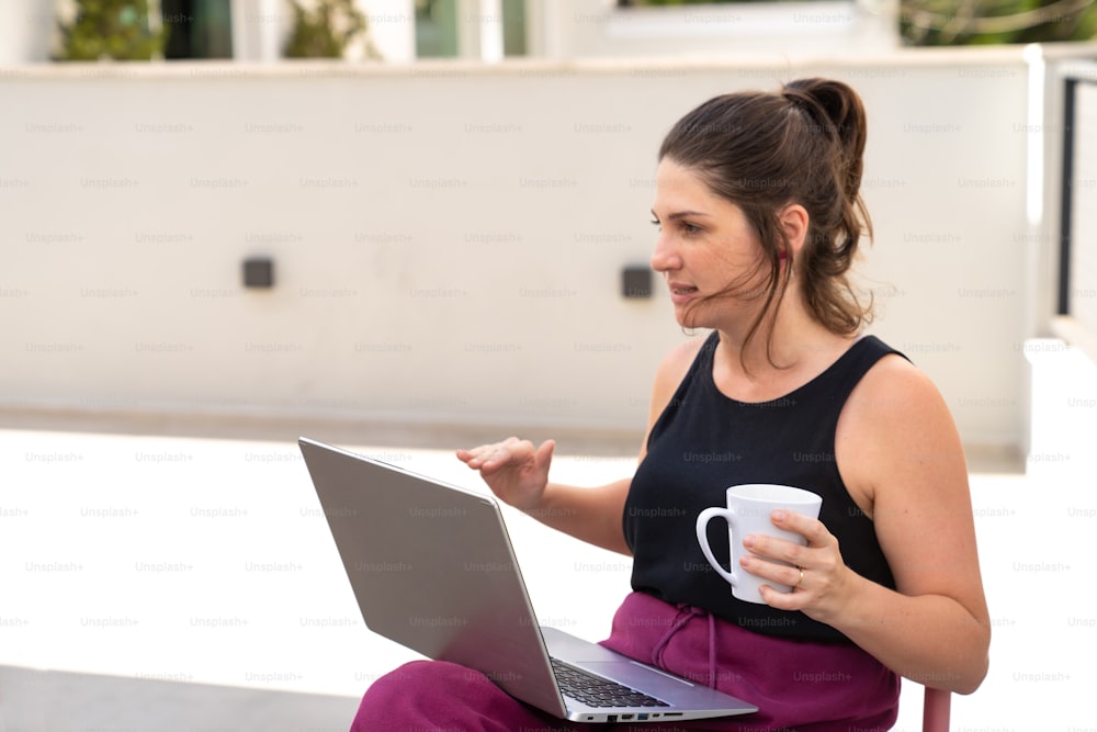 커피 컵과 노트북을 들고 의자에 앉아 있는 여자