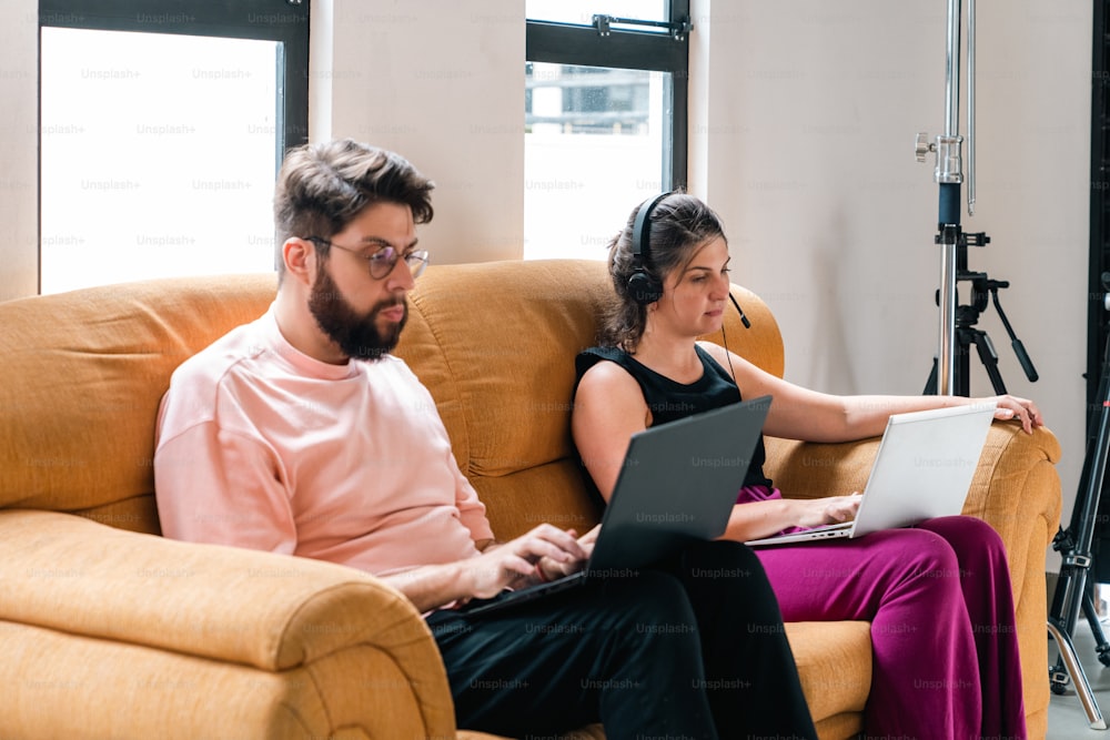 a man and a woman sitting on a couch looking at a laptop