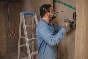 a man in a blue jacket and safety goggles working on a wall