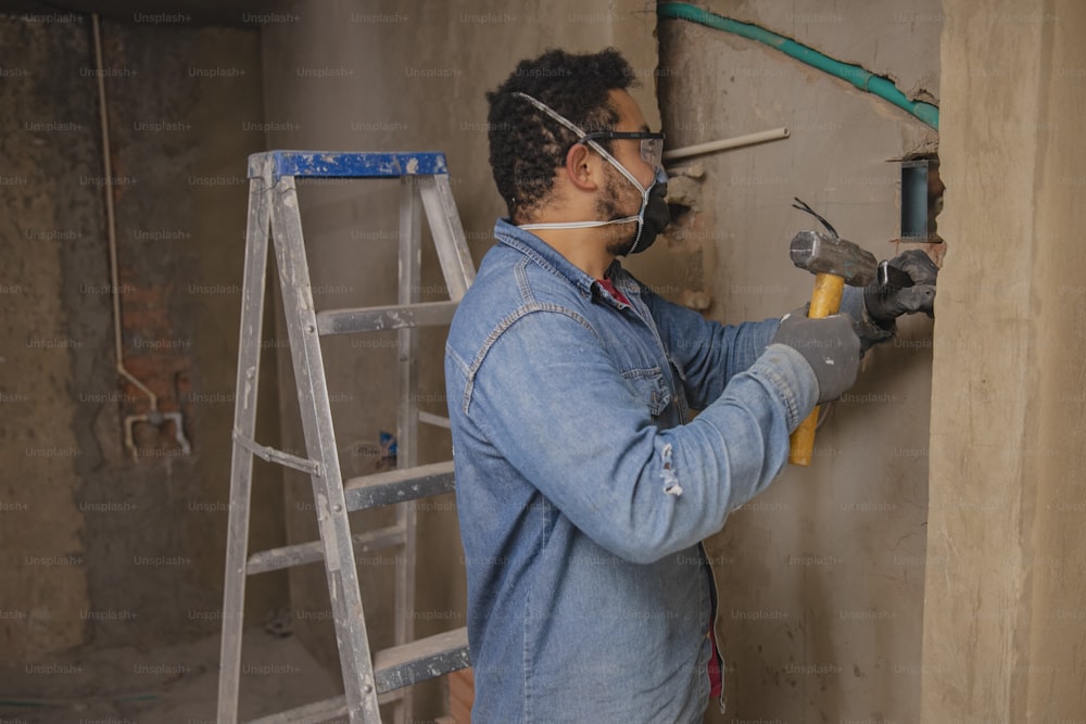 a man in a blue jacket and safety goggles working on a wall