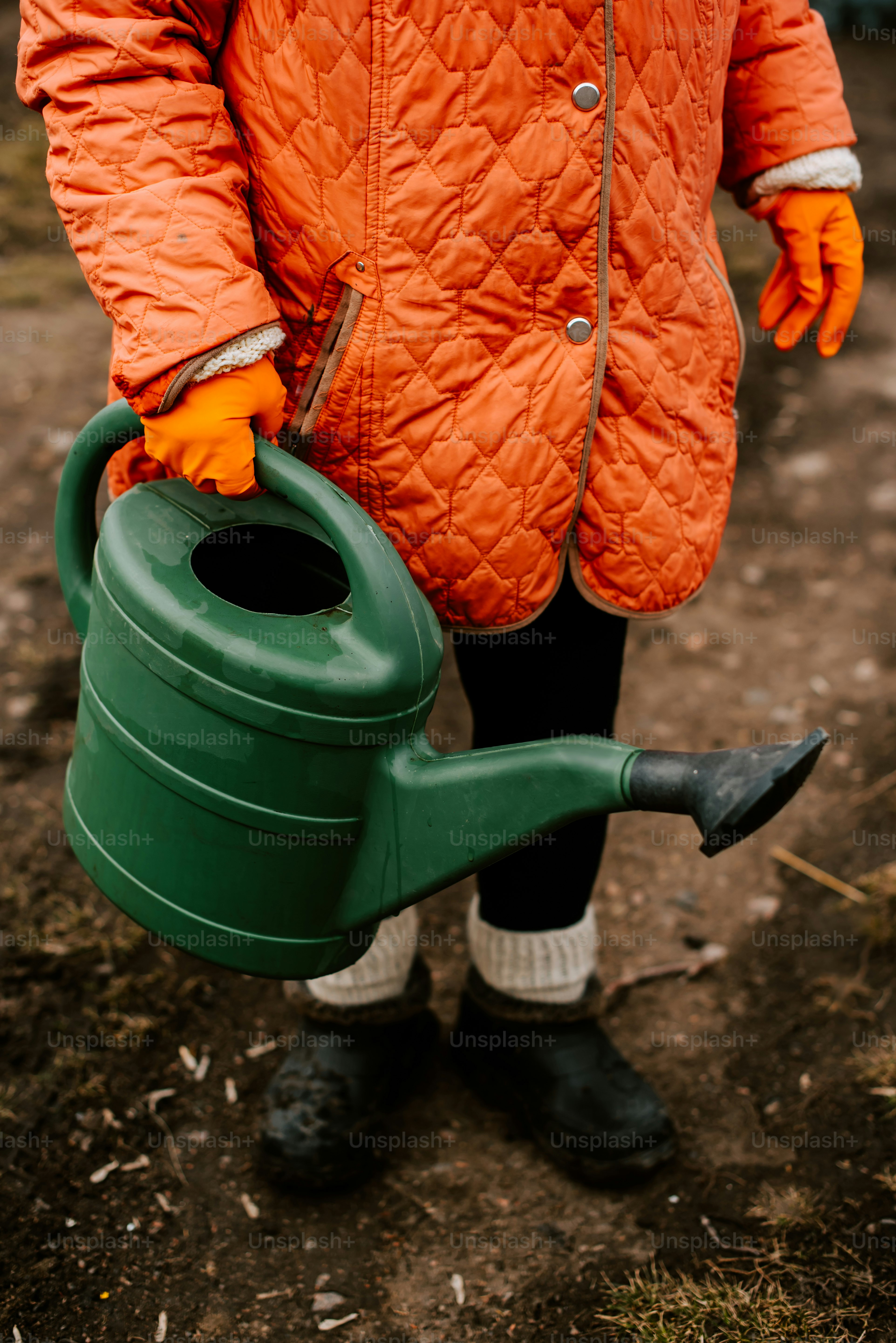 Una persona con una chaqueta naranja sosteniendo una regadera verde