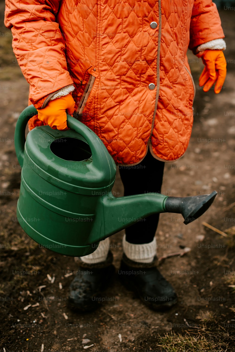 a person in an orange jacket holding a green watering can
