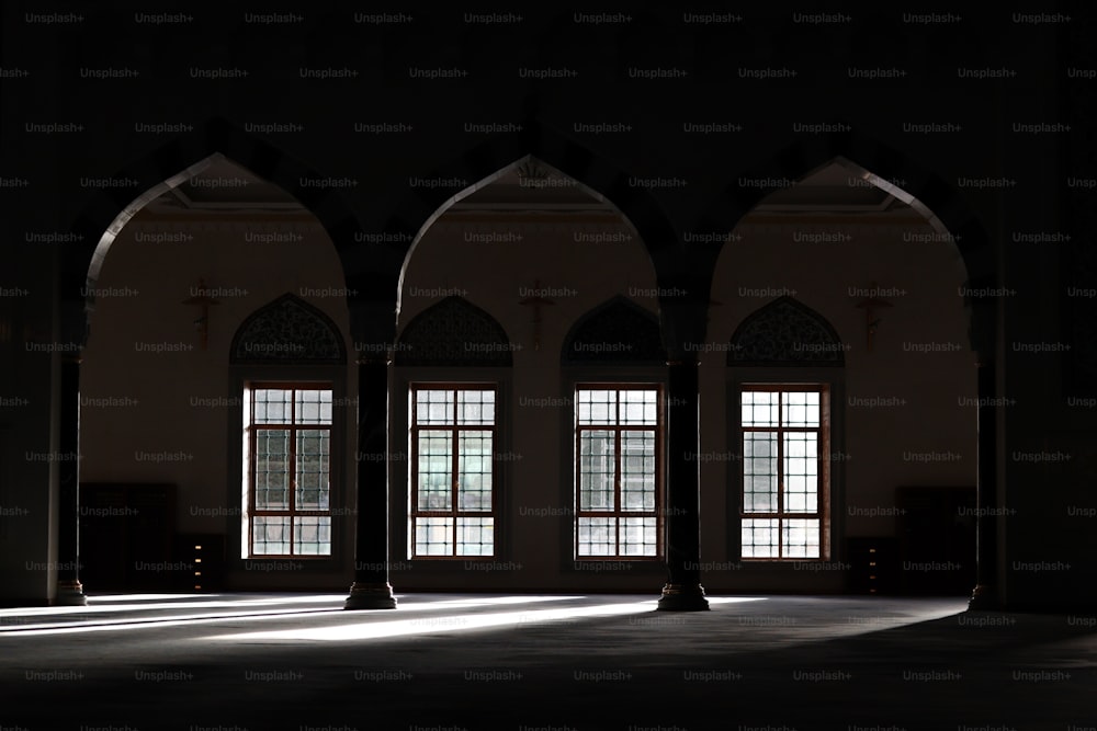 uma sala mal iluminada com três janelas e arcos