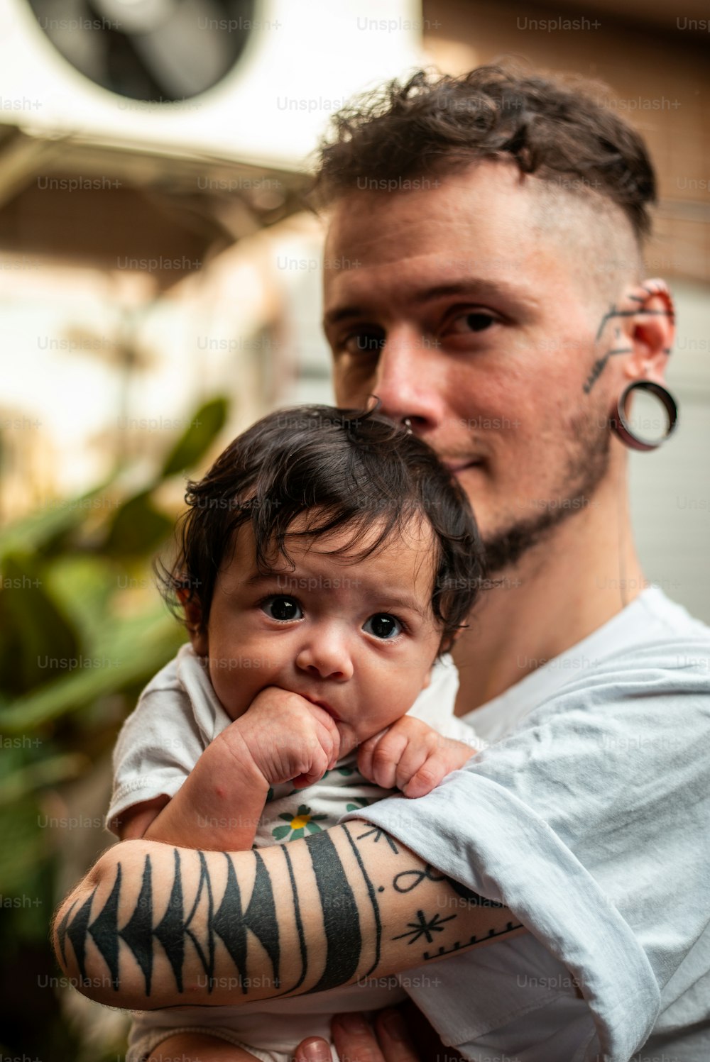 a man holding a baby with tattoos on his arms