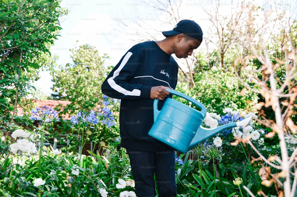 a man holding a blue watering can in a garden